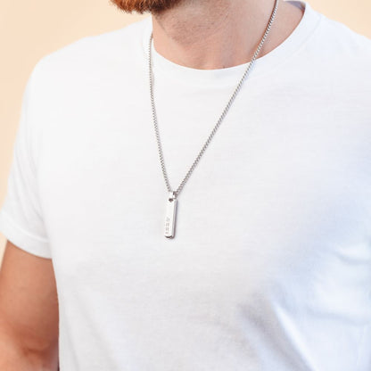 A man wearing a long silver pendant necklace 