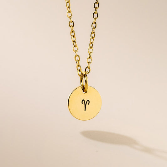 A gold-plated pendant necklace with a chain, featuring a round pendant with the zodiac sign for Aries engraved in the center.