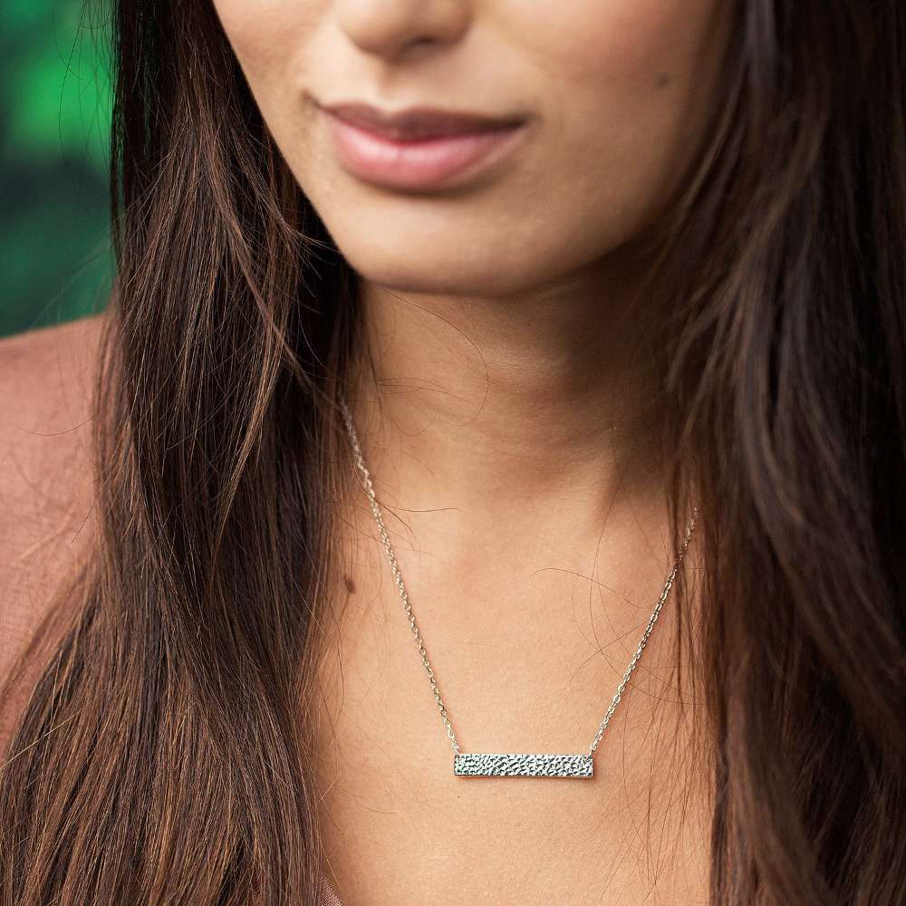 Close-up of a woman wearing a necklace with a bar pendant.