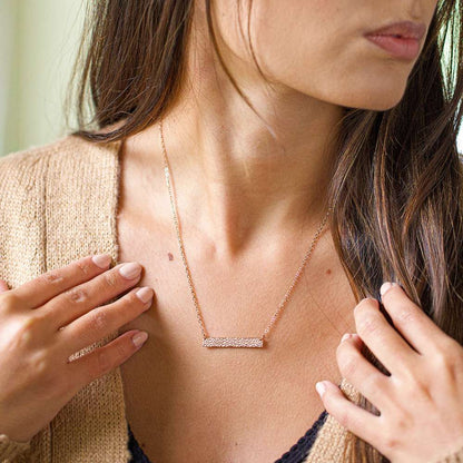 Woman wearing a gold necklace with her hands on her shoulders