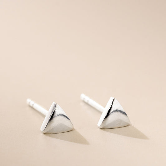 A pair of silver-colored fine triangle stud earrings on a beige background.