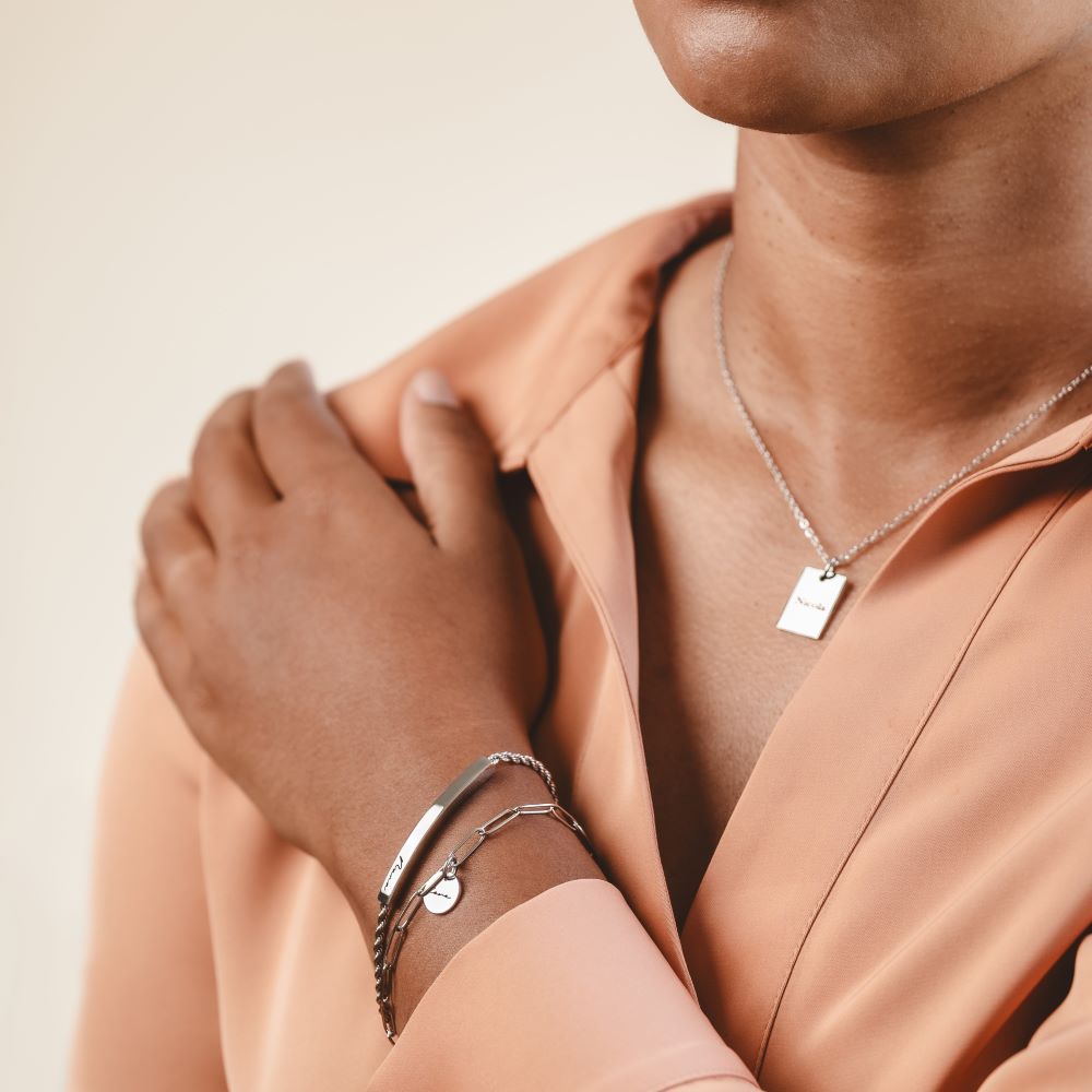 A woman wearing a stack of silver bracelets and an engraved necklace