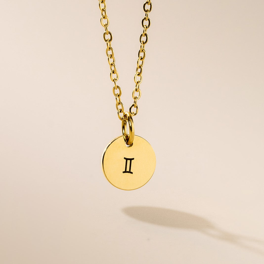 A gold-plated pendant necklace with a Gemini symbol on a chain, displayed against a neutral background.
