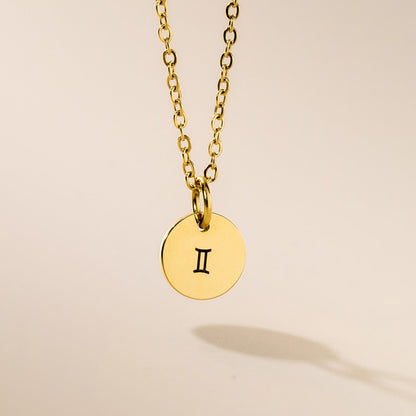 A gold-plated pendant necklace with a Gemini symbol on a chain, displayed against a neutral background.