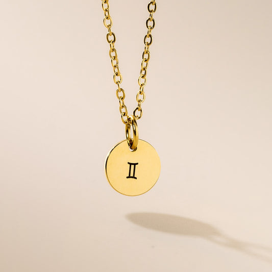 A gold-plated pendant necklace with a Gemini symbol on a chain, displayed against a neutral background.