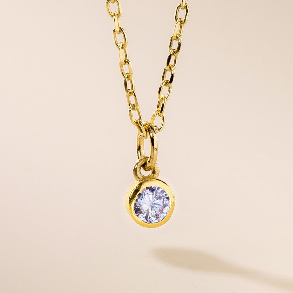 A gold-colored pendant featuring a clear, faceted birthstone surrounded by a chain.