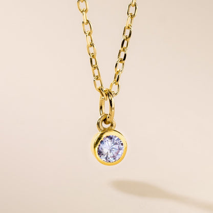 A gold-colored pendant featuring a clear, faceted birthstone surrounded by a chain.