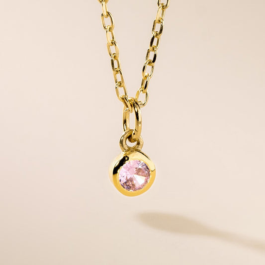 A gold-colored pendant featuring a pink birthstone gemstone.