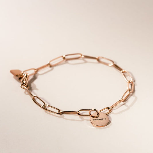 A rose gold bracelet with a chain link design and a pendant with a visible engraved initial 'M' on a white background.