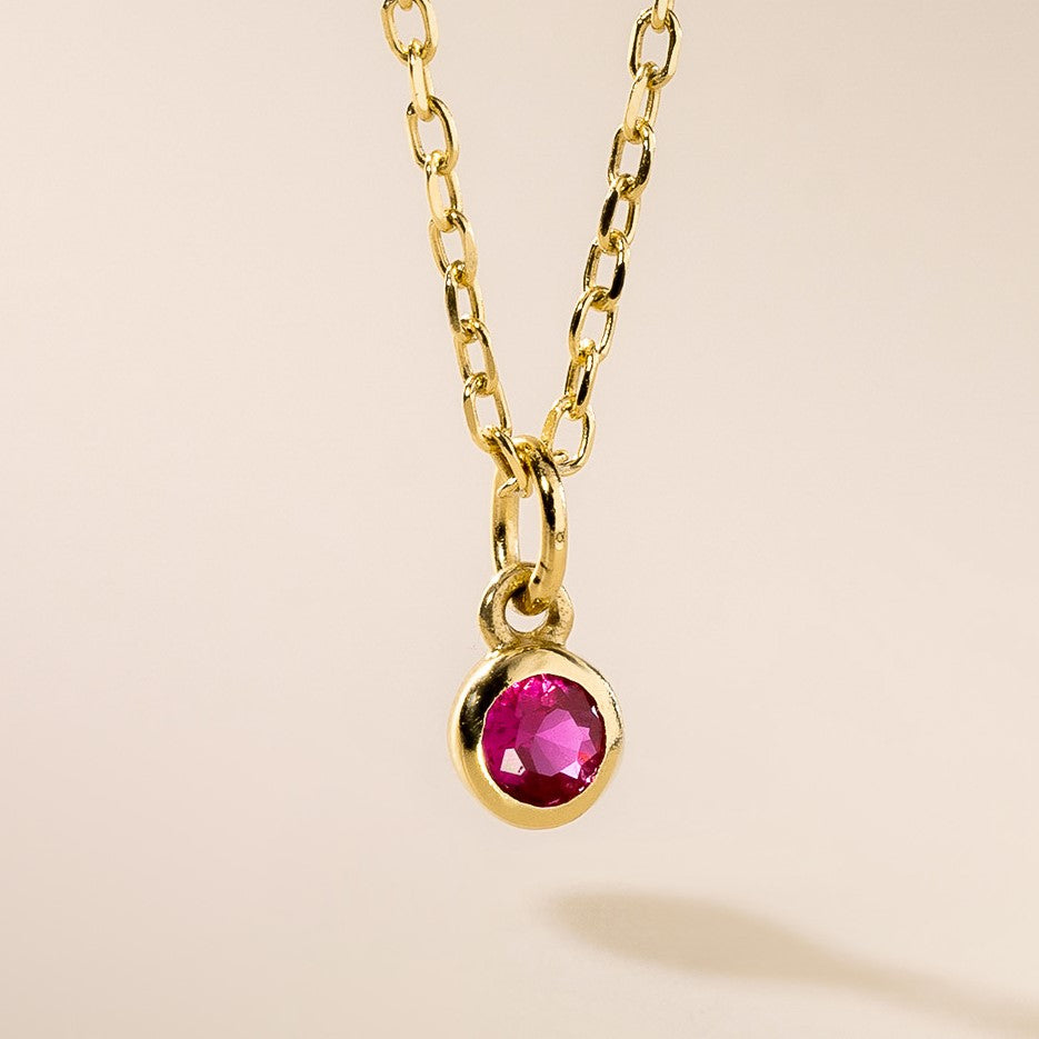 A gold pendant necklace with a round pink birthstone charm attached to a gold chain.