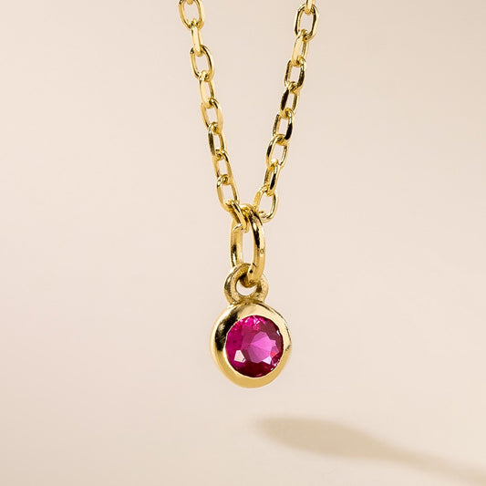 A gold pendant necklace with a round pink birthstone charm attached to a gold chain.