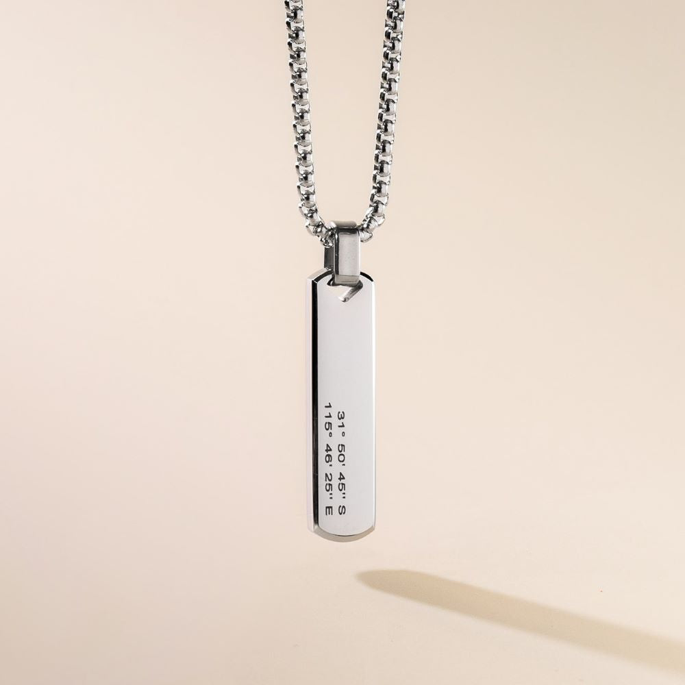 A sleek stainless steel pendant necklace with a bar-shaped pendant engraved with text, displayed against a neutral background.