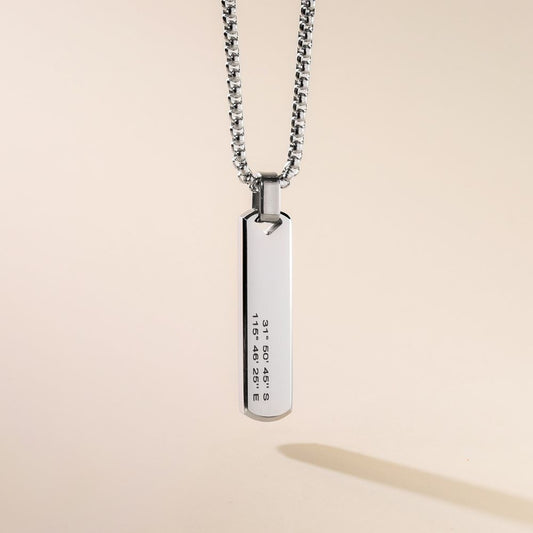 A sleek stainless steel pendant necklace with a bar-shaped pendant engraved with text, displayed against a neutral background.