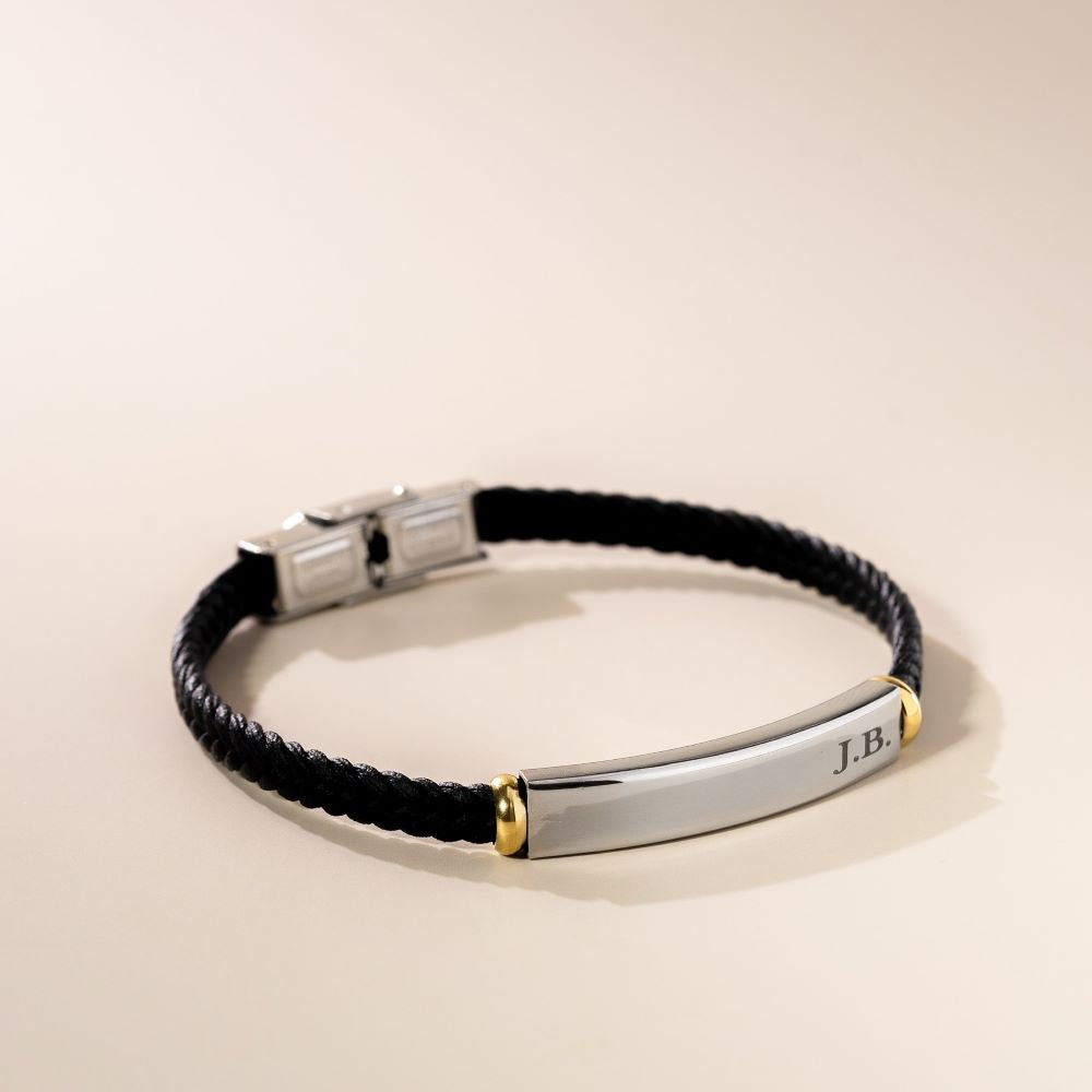 A leather rope bracelet with a metal clasp and an engraved metal plate. The bracelet is primarily black, and the metal is silver with gold accents.