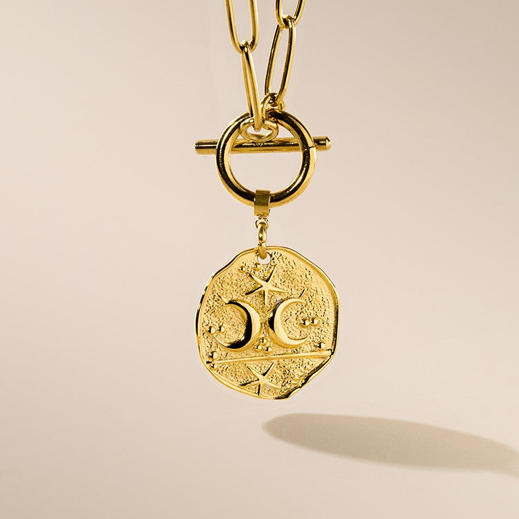 A gold-plated necklace with a crescent moon and star pendant, featuring a t-bar fastening.