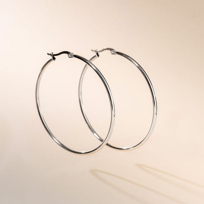 A pair of silver hoop earrings with a secure fastening, displayed against a beige background.