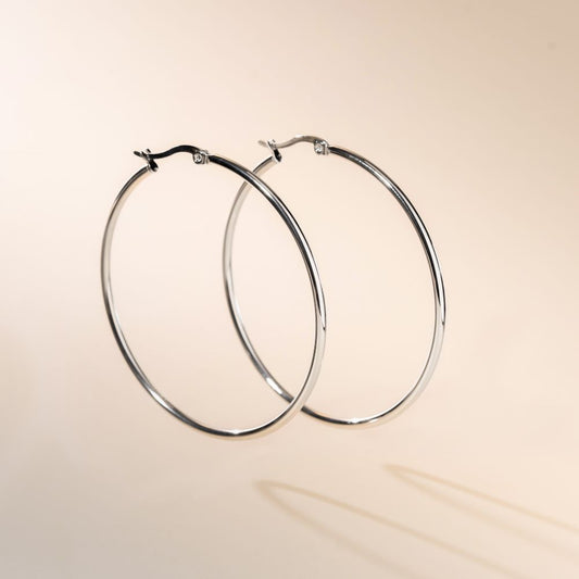 A pair of silver hoop earrings with a secure fastening, displayed against a beige background.