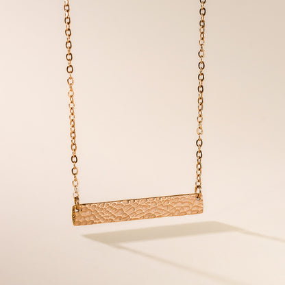 Gold necklace with a textured bar pendant on a beige background