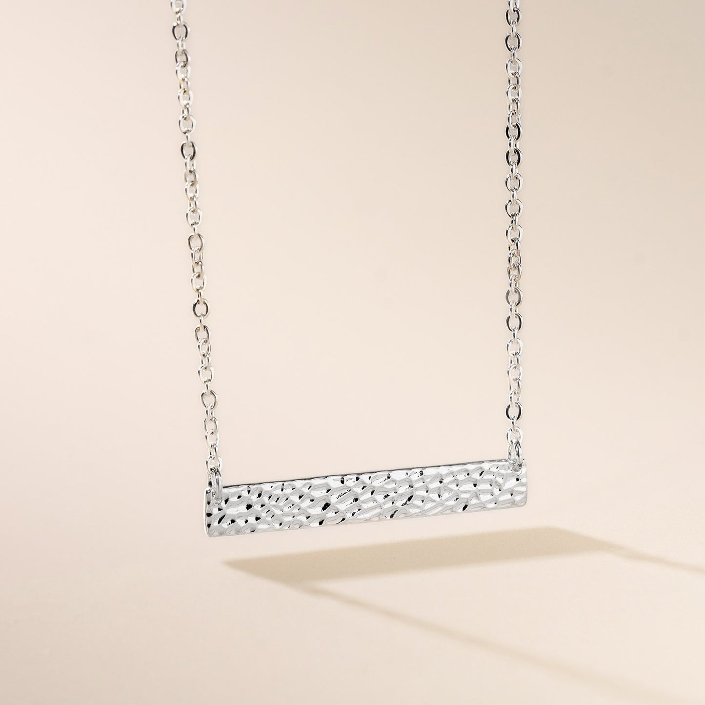 A silver hammered bar necklace on a chain, displayed against a neutral background.