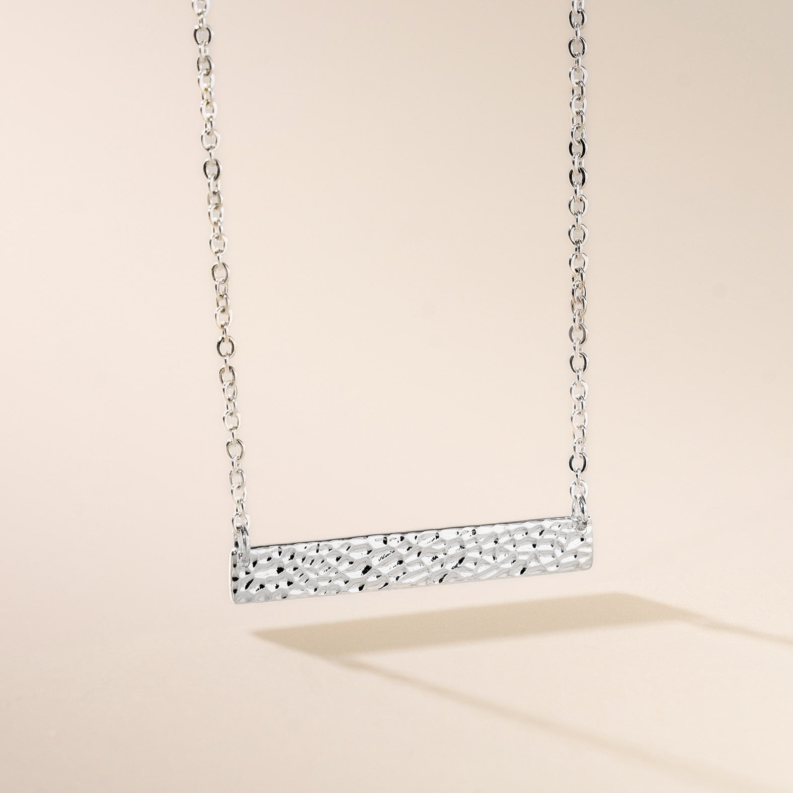 A silver hammered bar necklace on a chain, displayed against a neutral background.