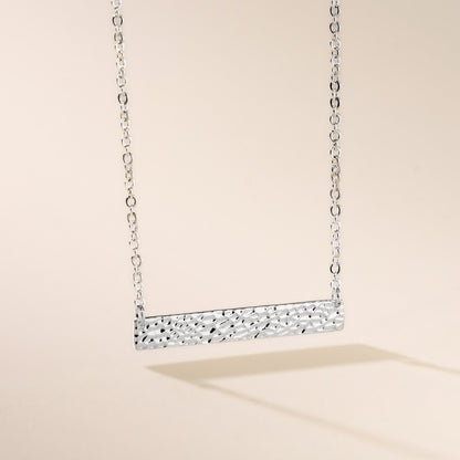 A silver hammered bar necklace on a chain, displayed against a neutral background.