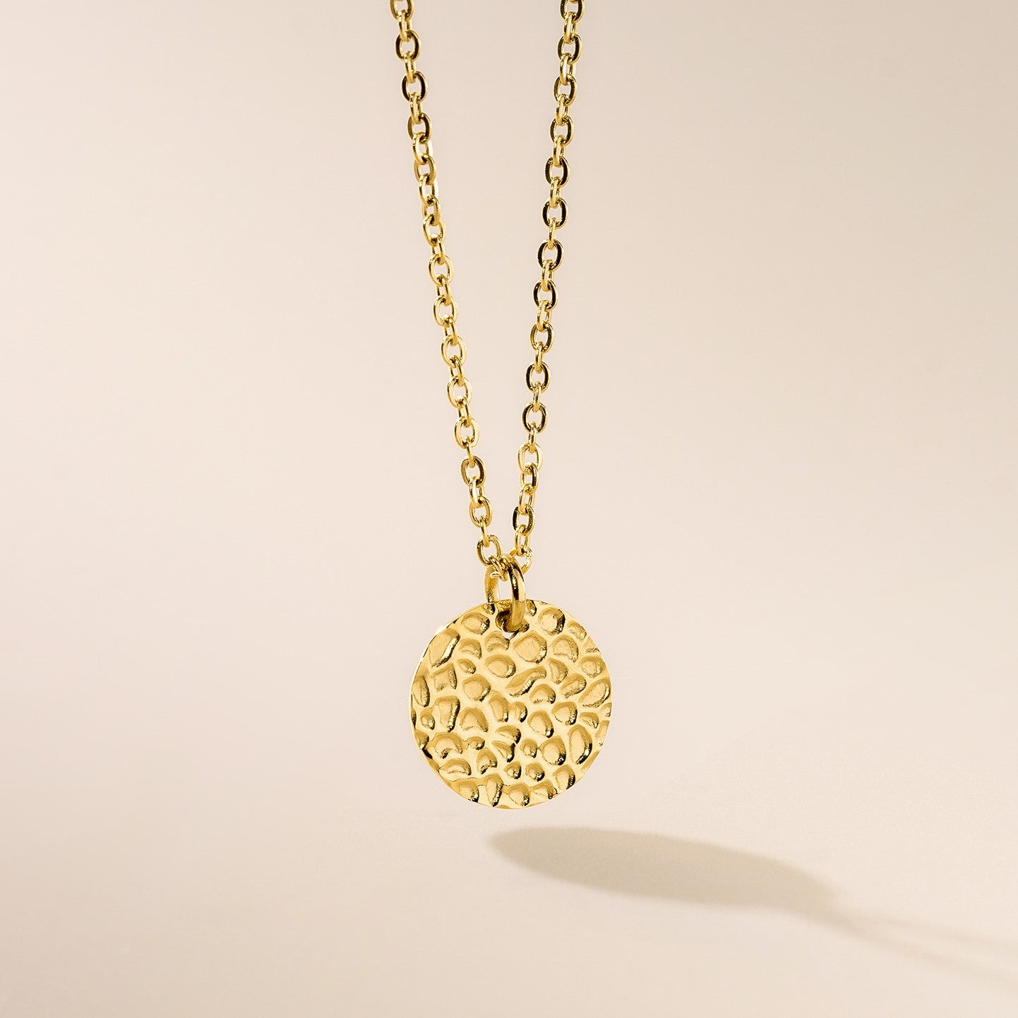 A gold hammered disc pendant necklace with a chain.