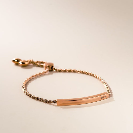 A rose gold rope bracelet with an adjustable slider and a bar for engraving, displayed against a neutral background.