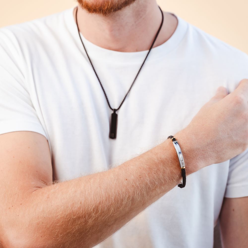 A man wearing a long black pendant necklace and a leather bracelet