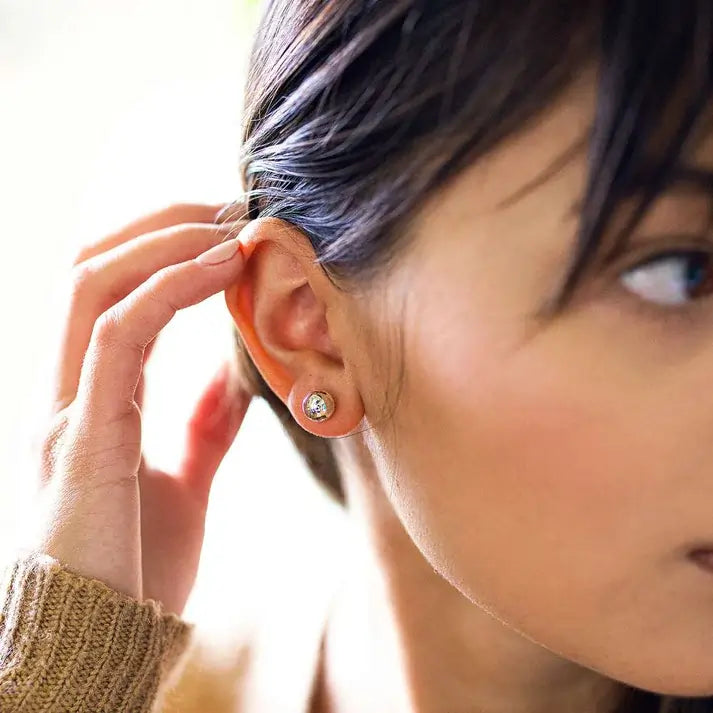 Close-up of a person wearing a ball stud earring with a blurred background