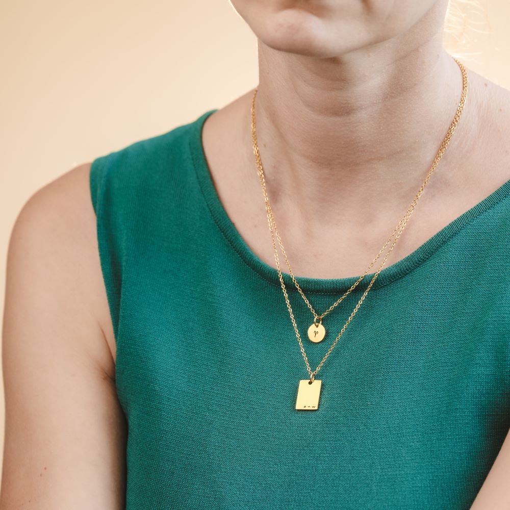 A woman wearing two golden necklaces with engraved pendants