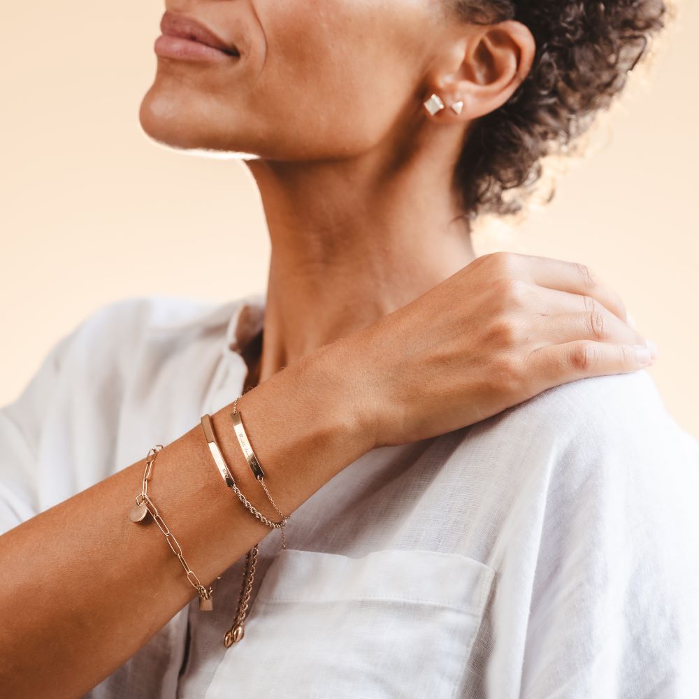 A woman wearing a stack of engraved bracelets in rose gold colour