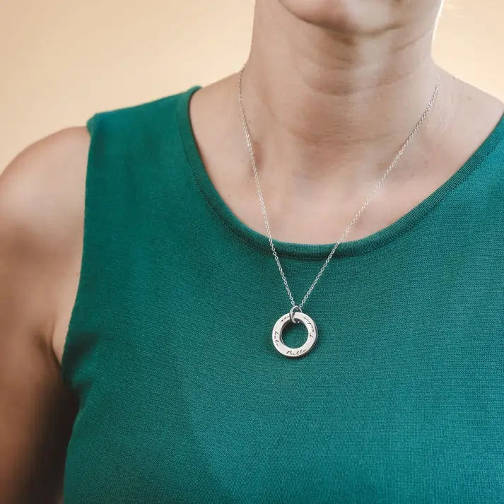 Person wearing a silver necklace with a circular pendant on a beige background
