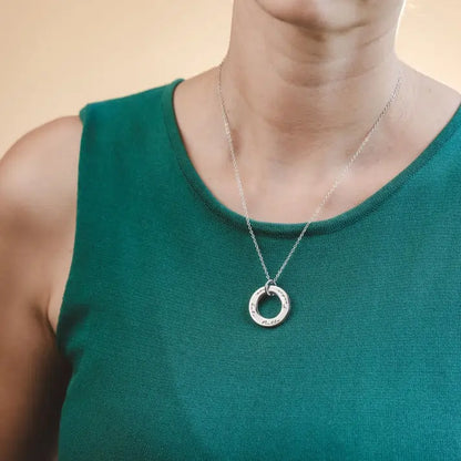 Person wearing a silver necklace with a circular pendant on a beige background