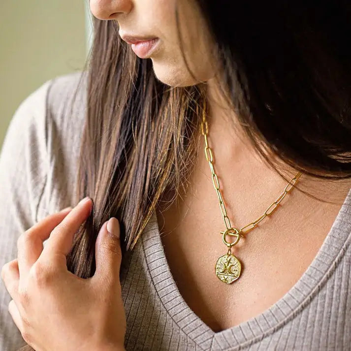 Woman wearing a gold necklace with a pendant, close-up of the necklace.