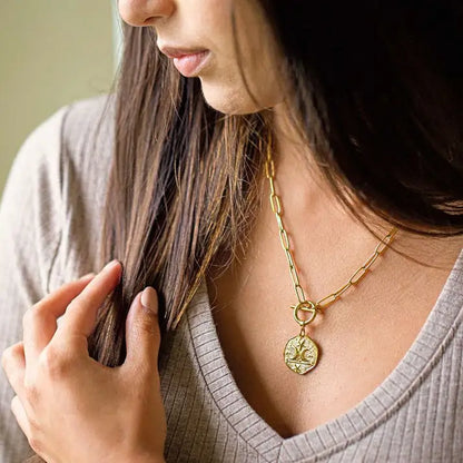 Woman wearing a gold necklace with a pendant, close-up of the necklace.