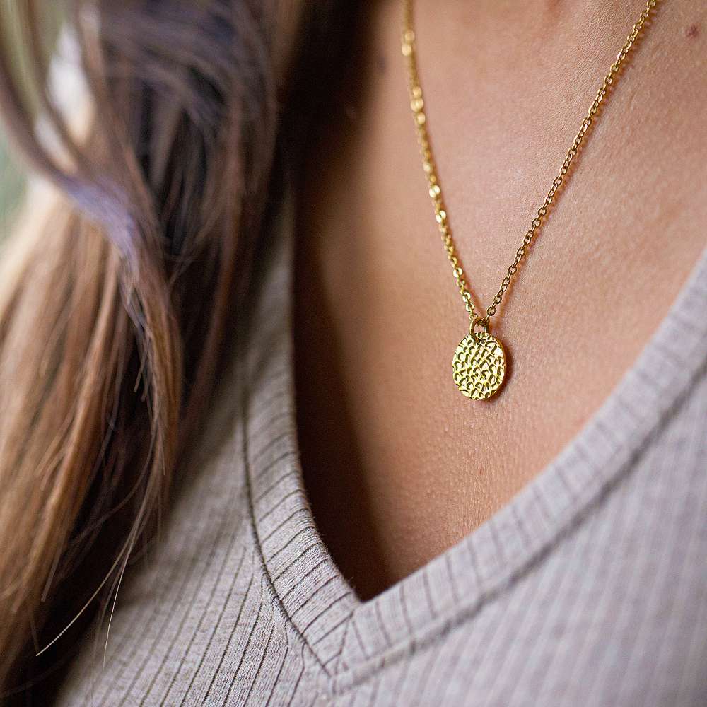 A girl wearing a gold hammered disc pendant necklace